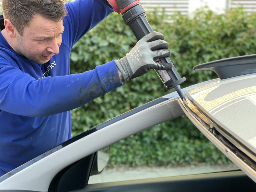 Un homme applique soigneusement de la colle pour réparer le pare-brise d'une voiture en extérieur à Copenhague.